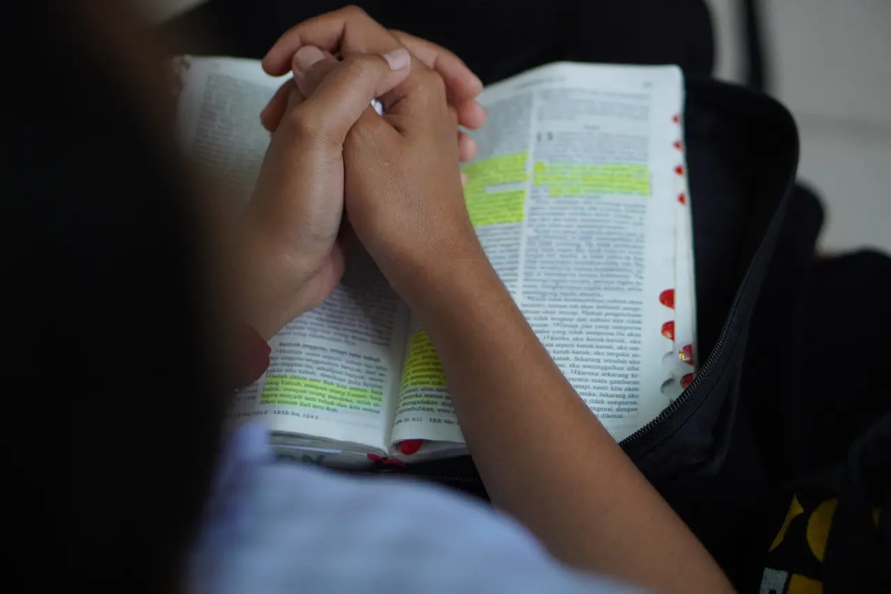 A person with an open Bible, hands folded in prayer